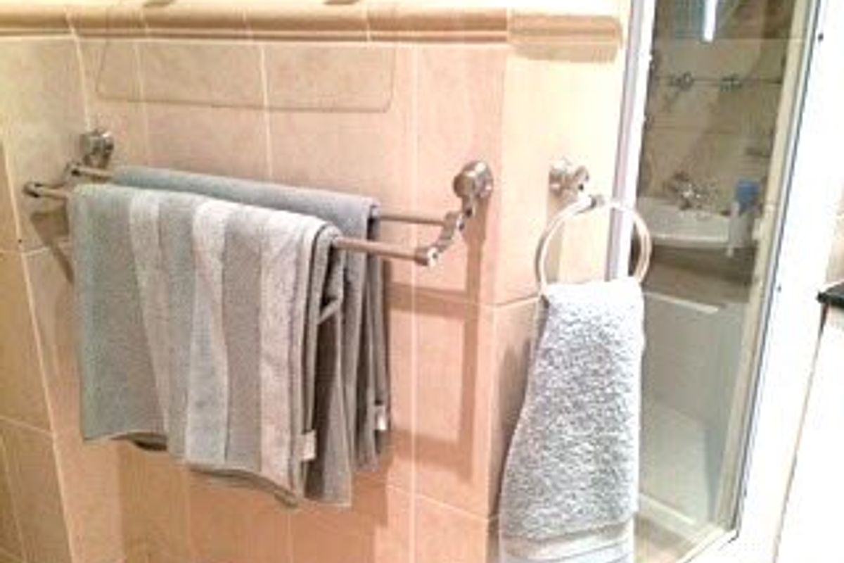 A bathroom featuring tiled walls, a double towel rail, a towel ring, and a glass-enclosed shower area.