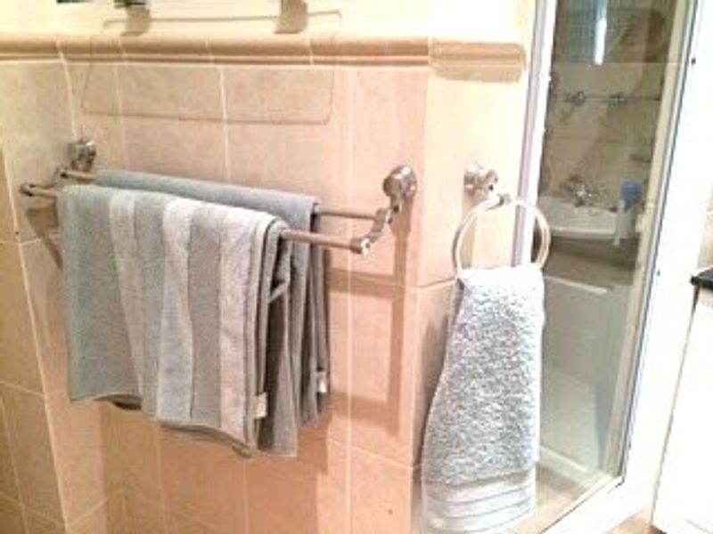 A bathroom featuring tiled walls, a double towel rail, a towel ring, and a glass-enclosed shower area.