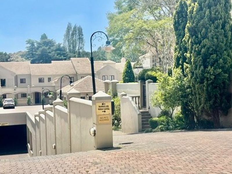 A view of the apartment complex entrance featuring a paved driveway, underground parking access, and well-maintained perimeter walls and landscaping.