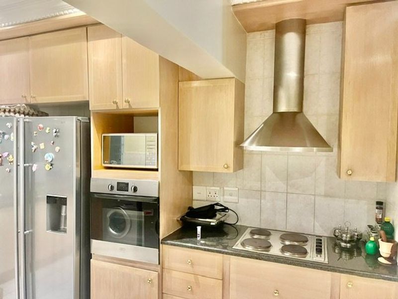 A functional kitchen featuring light wood cabinetry, granite countertops, a tiled backsplash, and integrated stainless steel appliances including an oven and extractor fan.