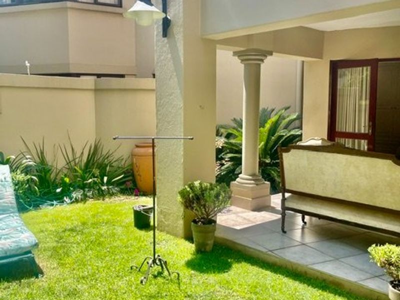 A private rear garden featuring a covered patio with tiled flooring, a classical column, and a well-maintained lawn area.
