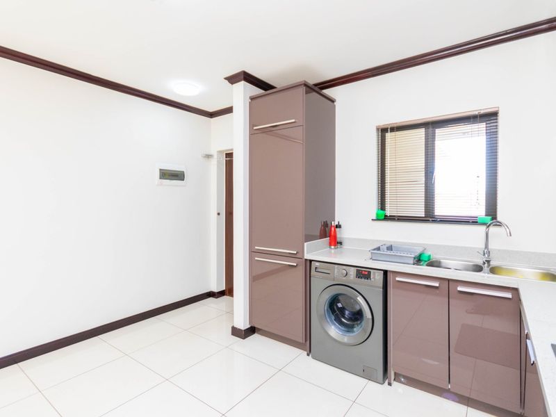 A clean and modern laundry area featuring sleek built-in cabinetry, stone countertops, a stainless steel sink, and tiled flooring.