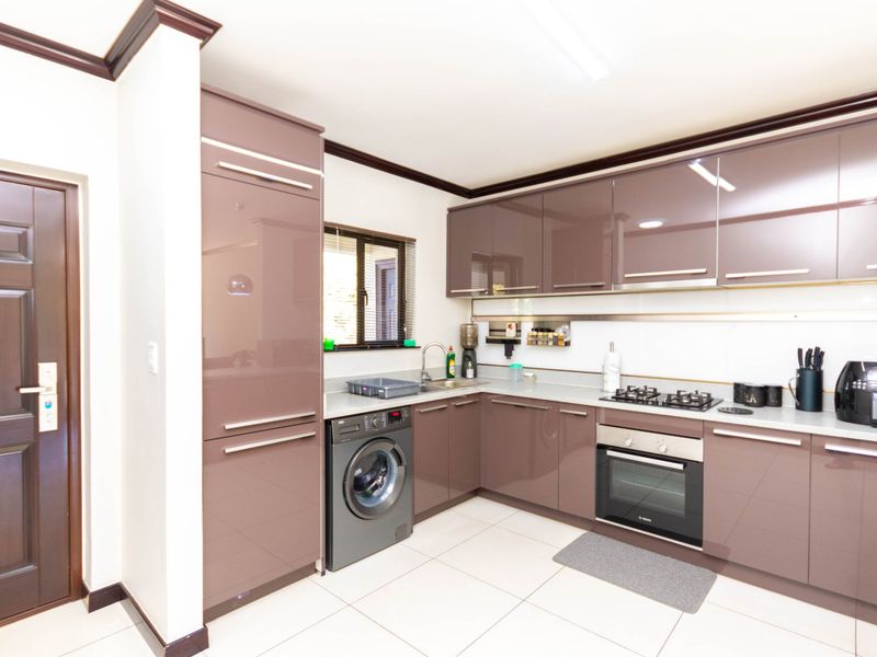 Modern kitchen featuring high-gloss cabinetry, built-in oven, gas hob, and integrated laundry facilities with tiled flooring and clean finishes.