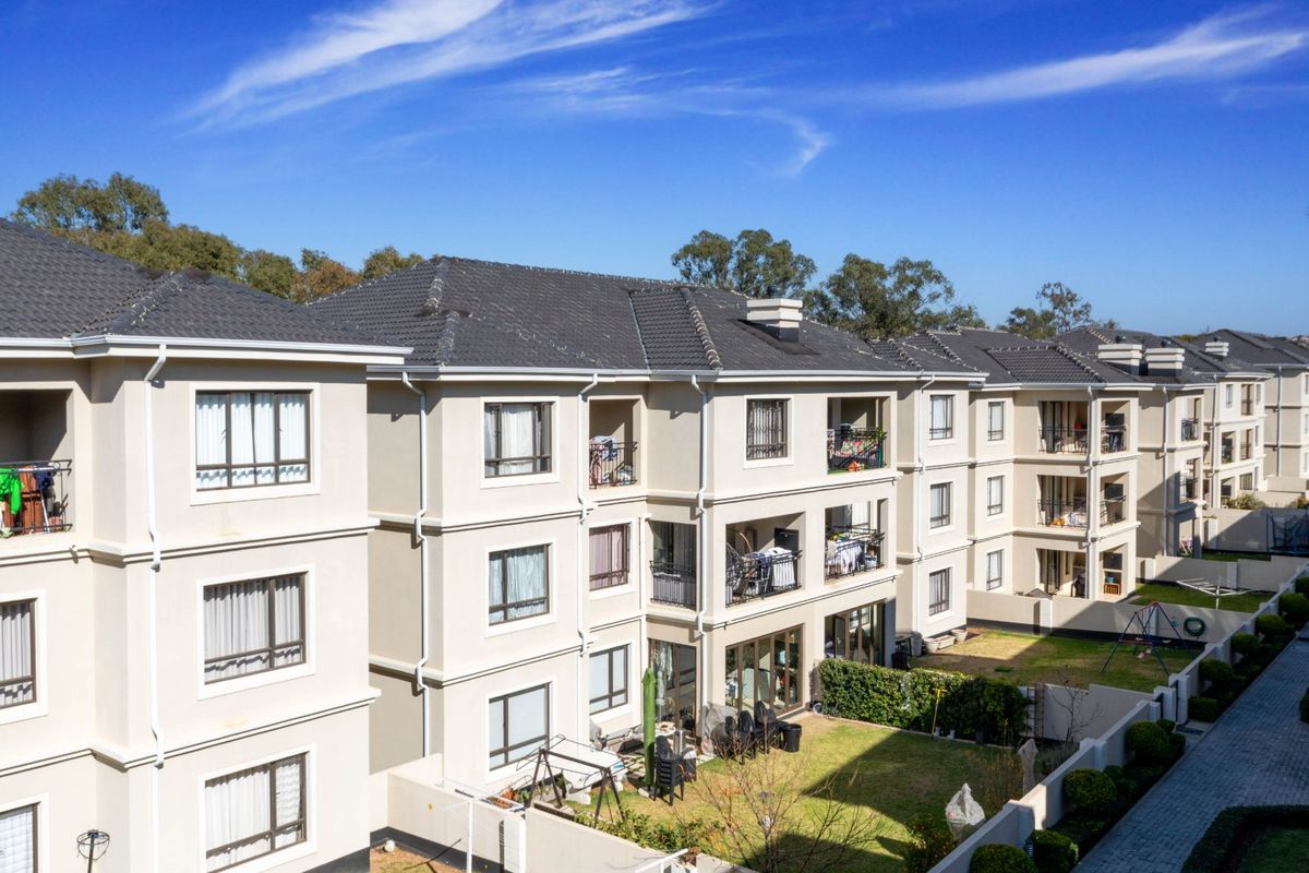 Aerial view of a modern multi-story apartment complex featuring tiled roofs, private balconies, and landscaped ground-floor garden areas.