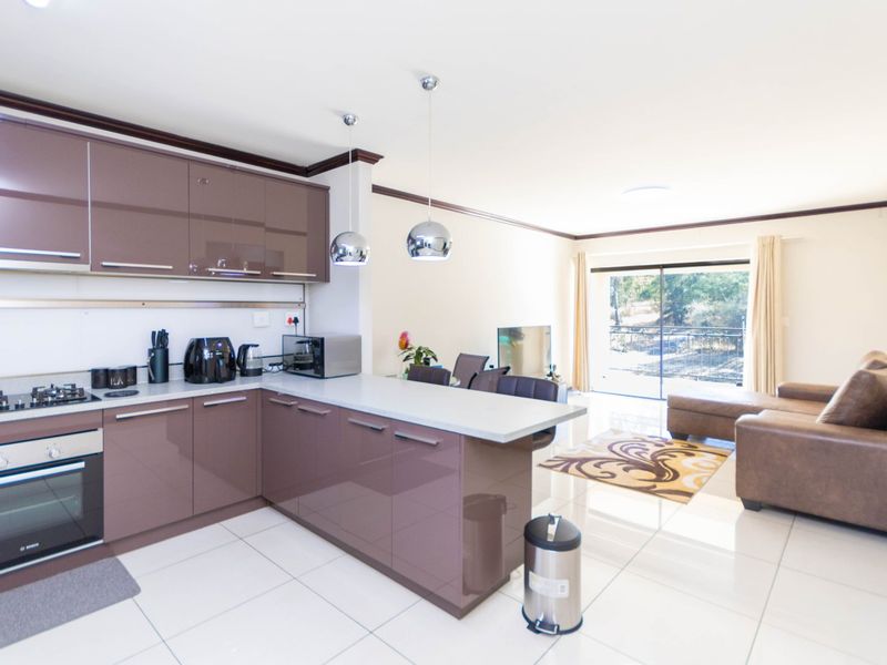 Modern open-plan kitchen and living area featuring high-gloss cabinetry, stone countertops, integrated appliances, and direct access to a balcony through sliding glass doors.