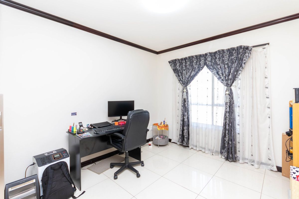 A functional bedroom featuring neutral tiled flooring and dark crown molding, providing a clean and versatile space for a home office or sleeping area.