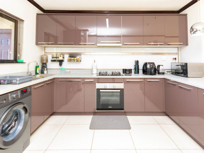 Modern kitchen featuring high-gloss cabinetry, stone countertops, built-in oven, gas hob, and integrated laundry appliance space with tiled flooring.