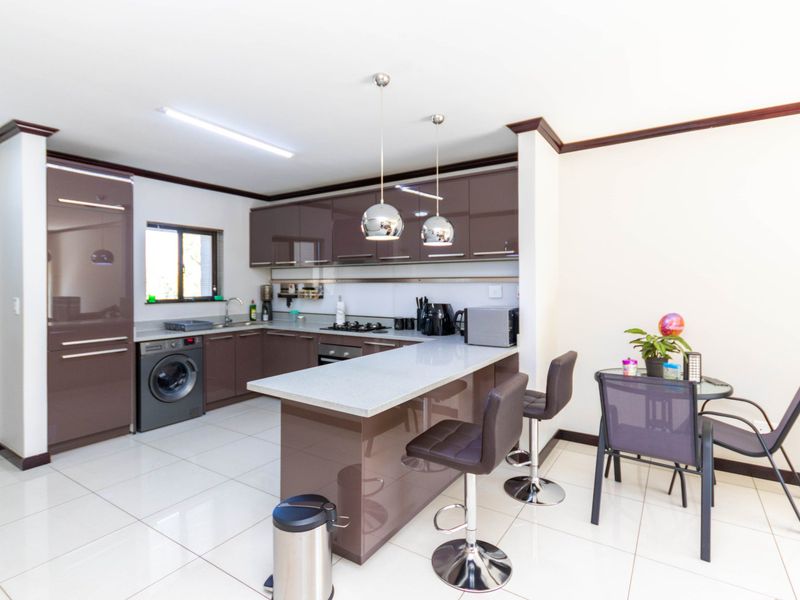 Modern open-plan kitchen featuring high-gloss cabinetry, stone countertops, a breakfast bar, and integrated appliances, seamlessly flowing into the dining area.