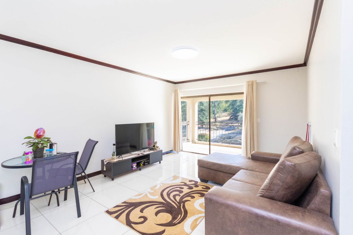 A bright living room featuring tiled flooring, crown molding, and a sliding glass door that opens onto a balcony.