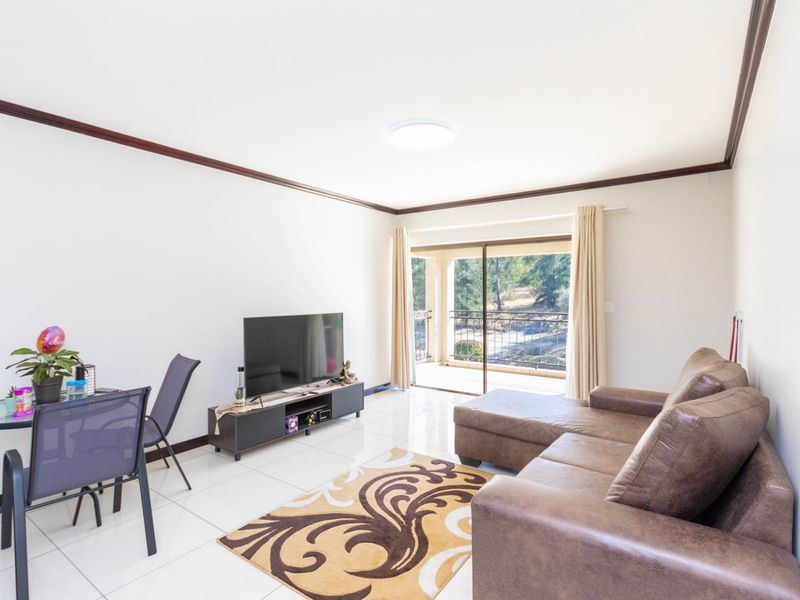 A bright living room featuring tiled flooring, crown molding, and a sliding glass door that opens onto a balcony.