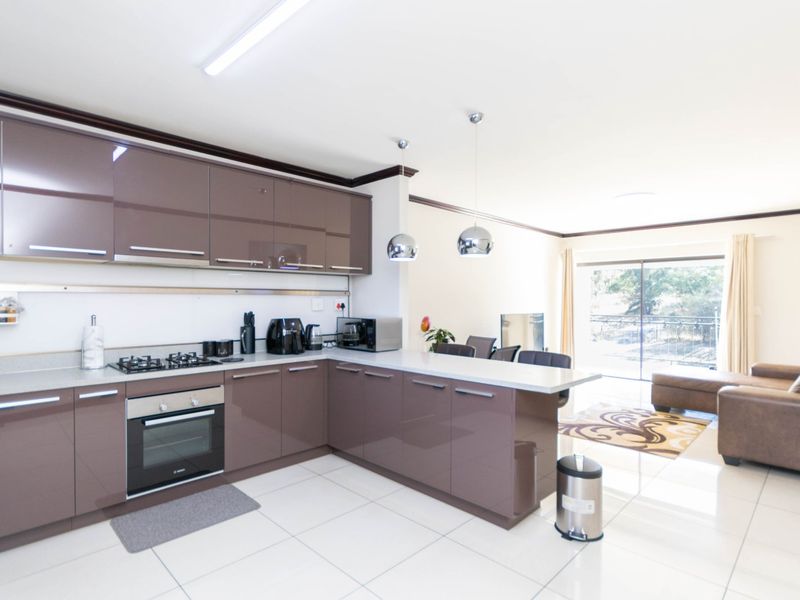Modern open-plan kitchen featuring high-gloss cabinetry, stone countertops, and integrated appliances, flowing seamlessly into a bright living area with access to a balcony.