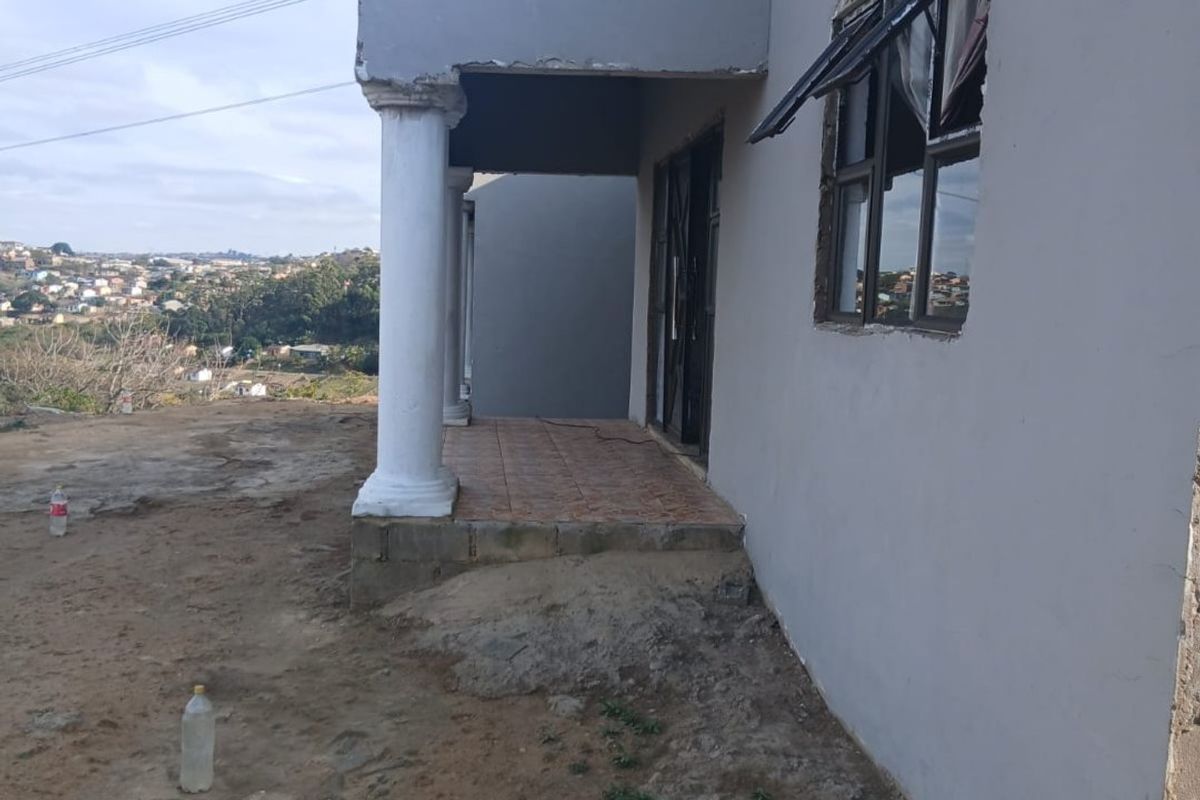 Rear exterior view of the house featuring a covered patio with concrete columns, tiled flooring, and unfinished exterior wall finishes.