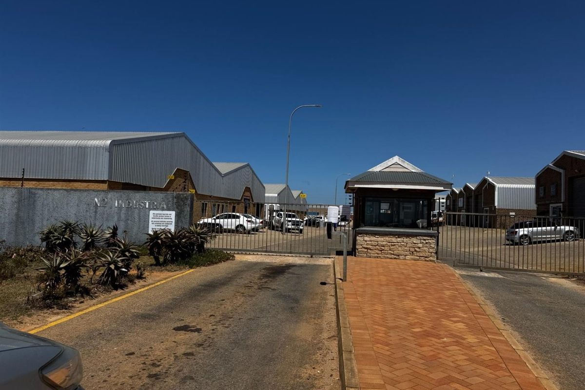 Front entrance view of the N2 Industria complex, featuring a secure gated access point, guard house, and paved driveway leading to industrial warehouse units.