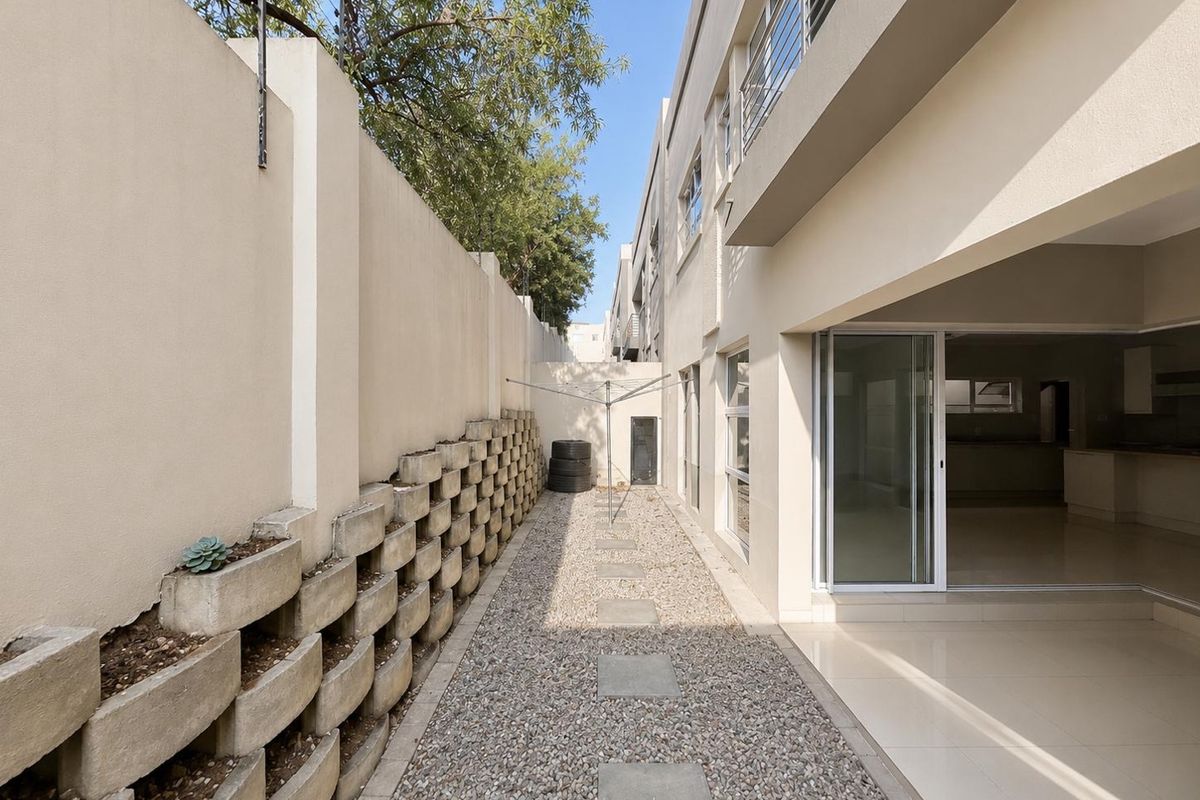 A narrow rear exterior side passage featuring a gravel pathway, concrete retaining wall with integrated planters, and access to the main living area via sliding doors.