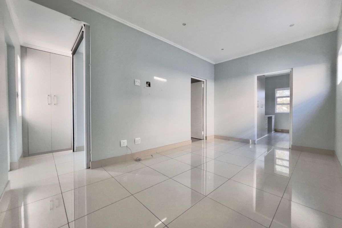 A bright, empty bedroom featuring neutral tiled flooring, built-in cupboards, and recessed lighting, offering a clean and versatile space.
