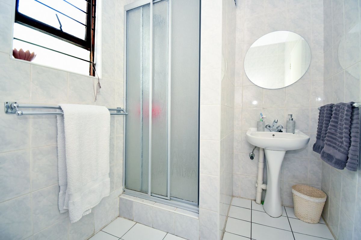 A functional bathroom featuring a pedestal basin, shower enclosure, and neutral wall and floor tiling, providing a clean and practical space.