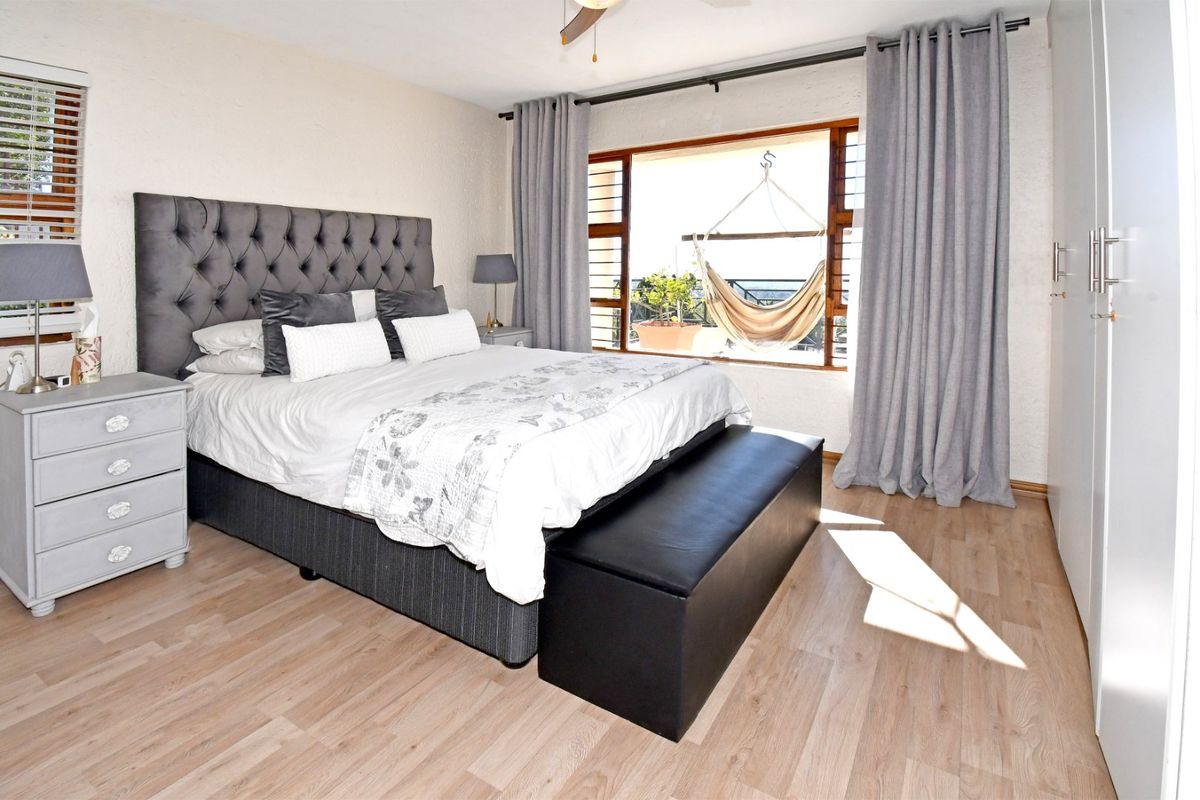 A well-lit bedroom featuring laminate flooring, a built-in wardrobe, and large windows with access to an outdoor balcony area.