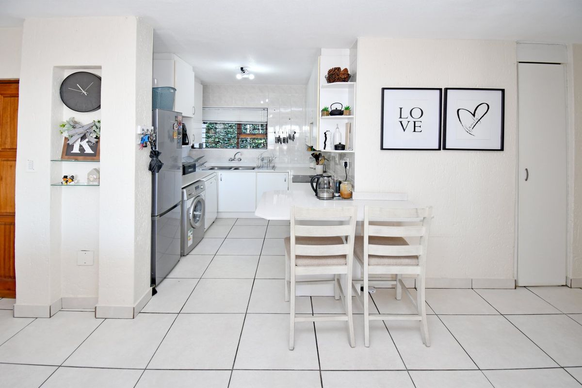 A functional kitchen featuring white cabinetry, tiled flooring, a double sink, and an integrated breakfast counter, offering a clean and practical layout.