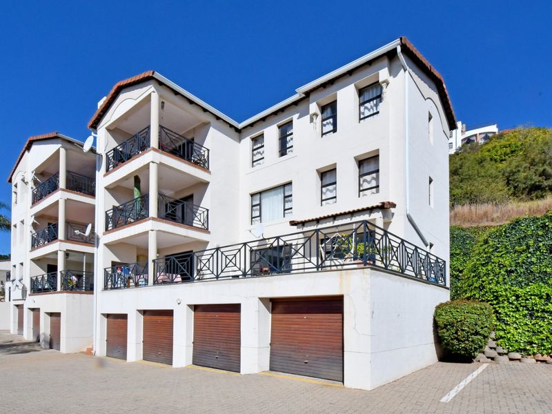 Exterior view of a multi-story apartment complex featuring covered balconies with wrought iron railings and ground-level garage access.