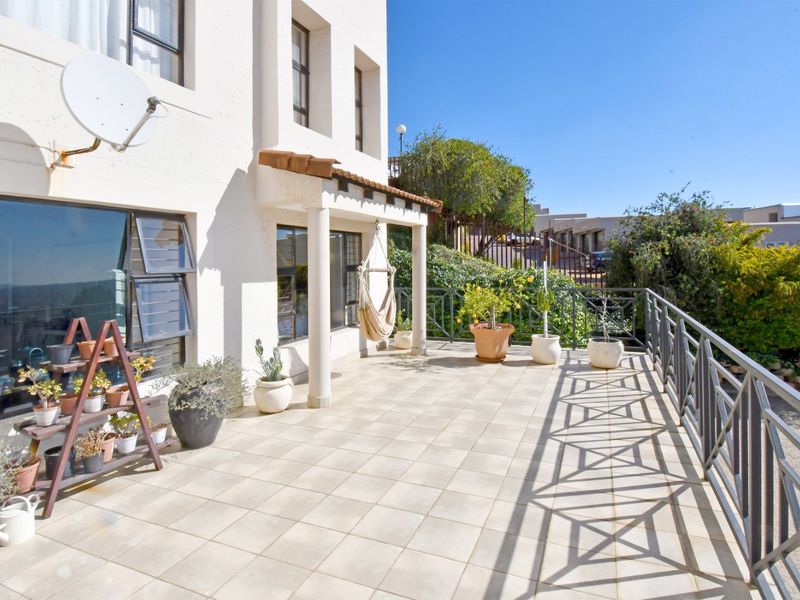 A spacious tiled balcony featuring a metal balustrade, covered porch area, and direct access to the apartment interior.