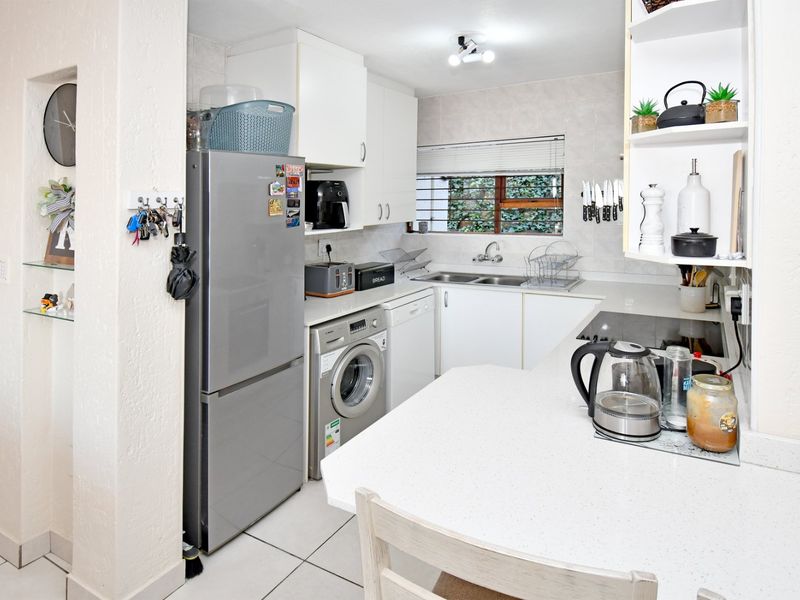 A functional kitchen featuring white cabinetry, tiled backsplash, double sink, and tiled flooring with a breakfast bar counter.