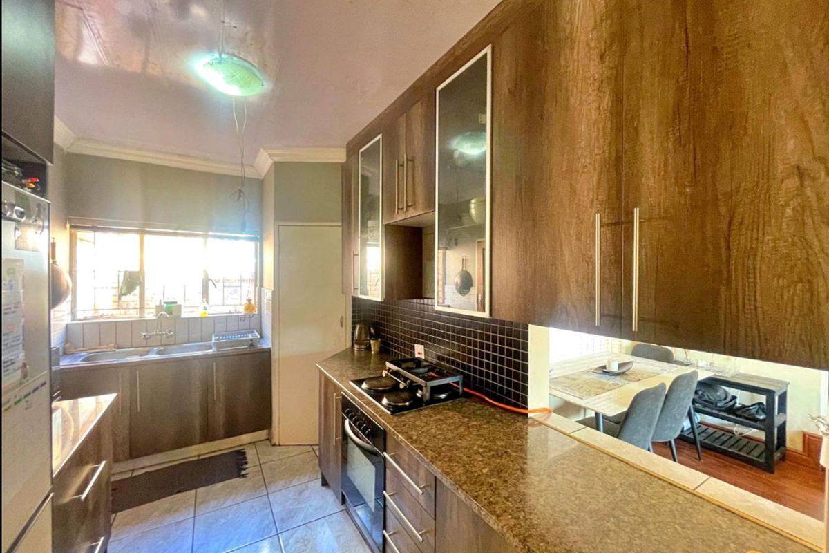 A functional kitchen featuring dark wood-look cabinetry, granite-style countertops, a gas hob, built-in oven, and a double basin sink with tiled backsplash.