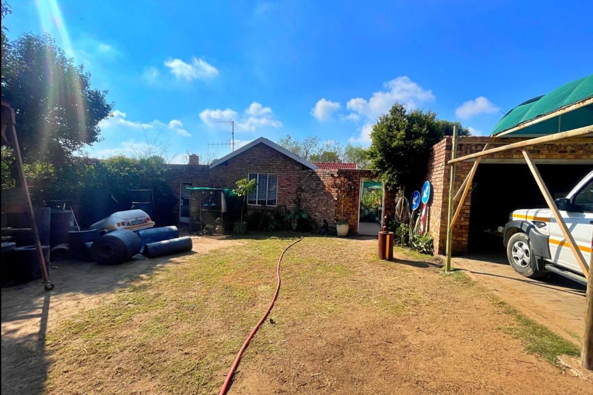 Rear view of the property featuring a brick facade, a carport structure, and a spacious garden area.