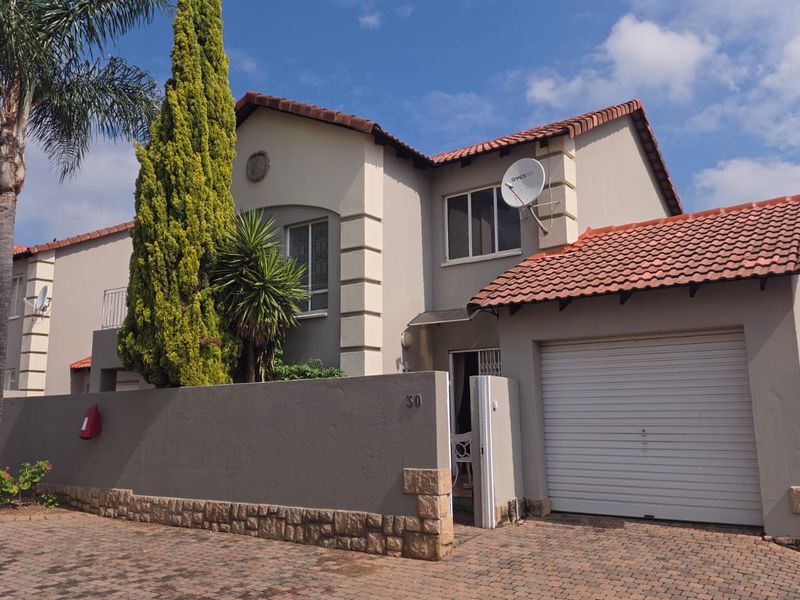 Front elevation of a two-story apartment unit featuring a tiled roof, integrated garage, and a private boundary wall with stone cladding accents.
