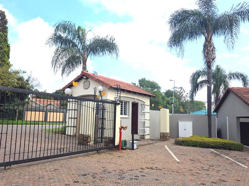 Front entrance of the apartment complex featuring a secure gated access point, guard house, and paved driveway area.
