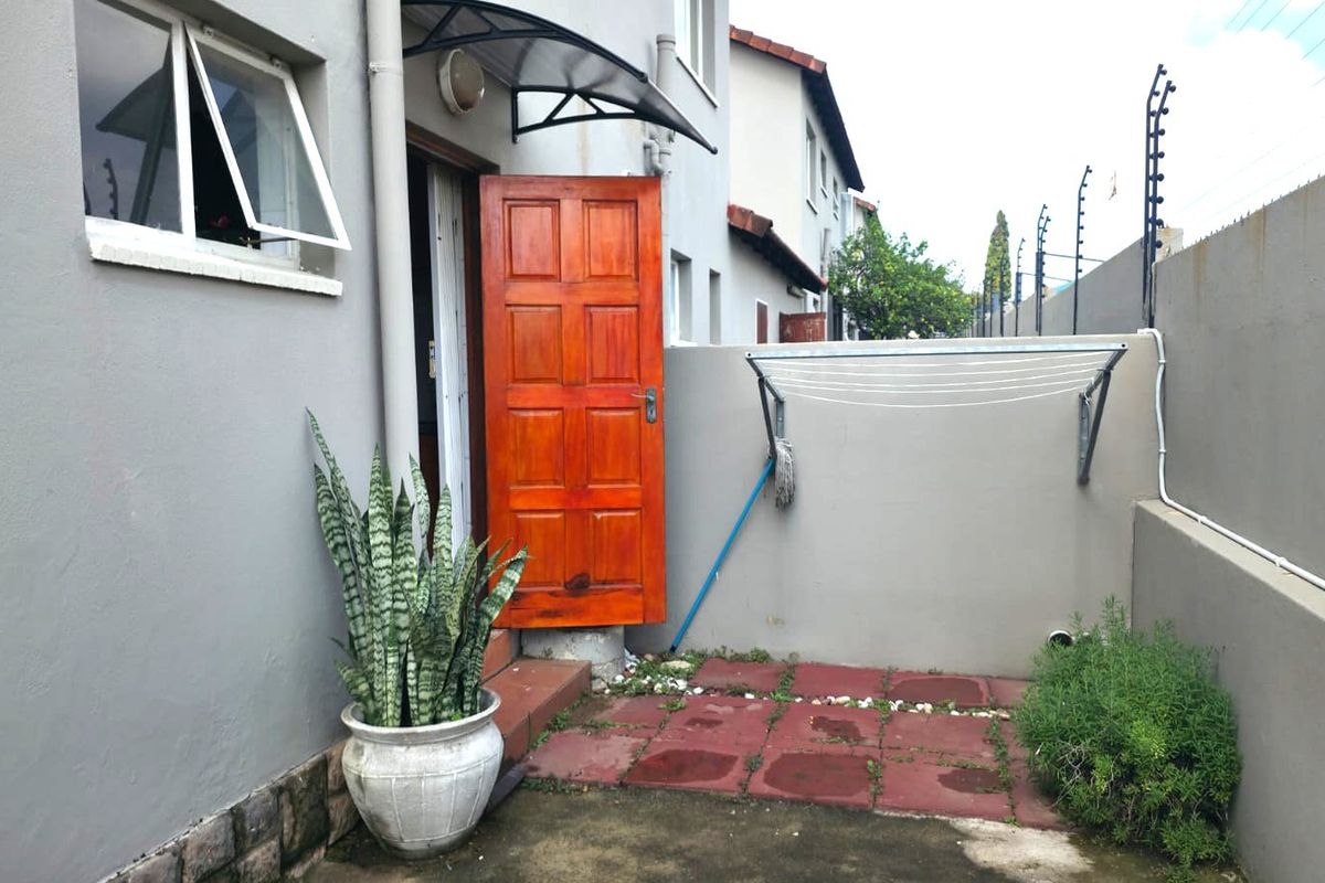A rear exterior area featuring a paved patio, boundary wall with electric fencing, and a small entrance awning.