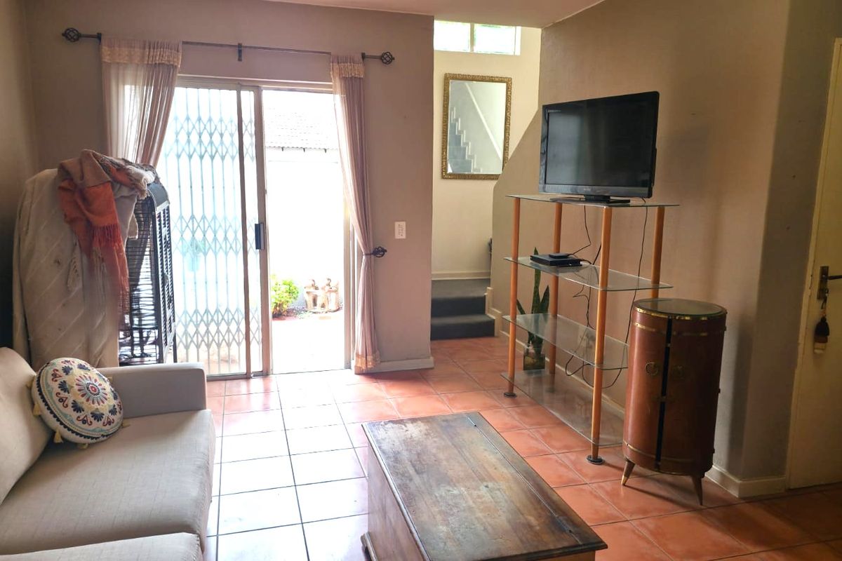 A living room featuring tiled flooring and a sliding glass door leading to an outdoor area, with an adjacent staircase leading to the upper level.