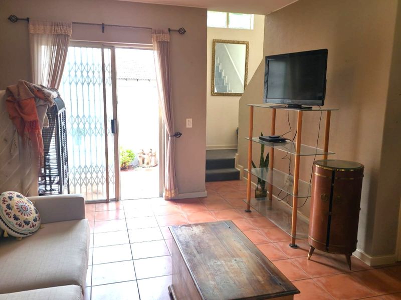 A living room featuring tiled flooring and a sliding glass door leading to an outdoor area, with an adjacent staircase leading to the upper level.