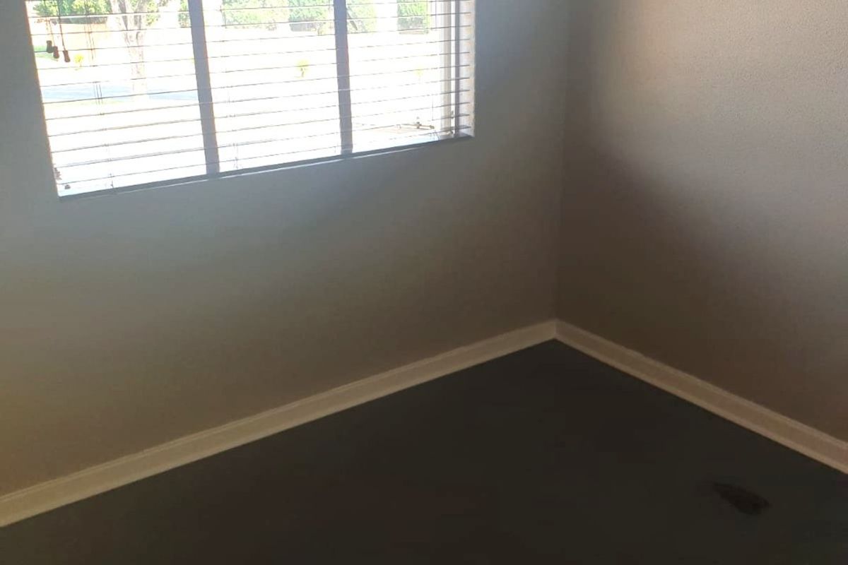 An empty bedroom featuring neutral wall paint, dark carpeting, and fitted venetian blinds, offering a blank canvas for personalization.
