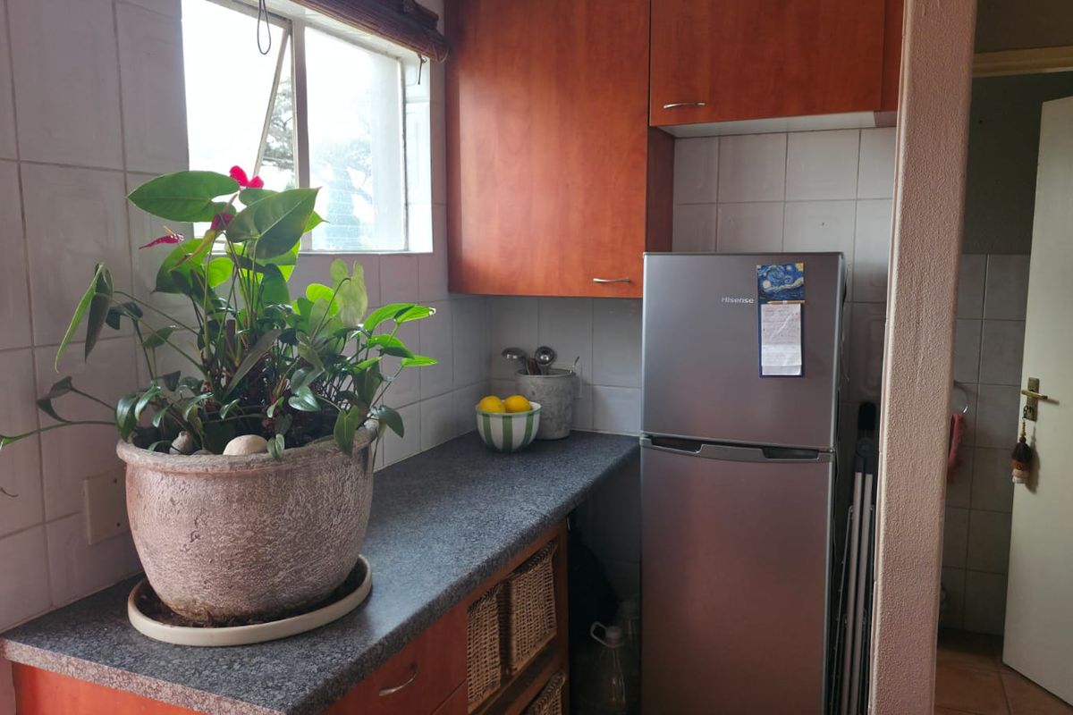 A compact kitchen area featuring wood-tone cabinetry, stone-look countertops, and tiled splashbacks, providing a functional prep space with natural light.