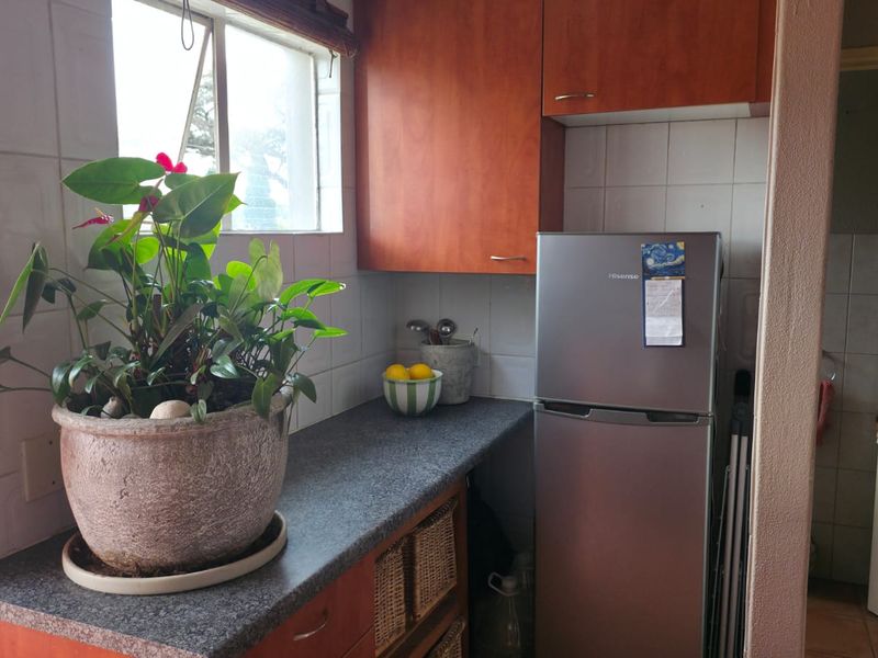 A compact kitchen area featuring wood-tone cabinetry, stone-look countertops, and tiled splashbacks, providing a functional prep space with natural light.
