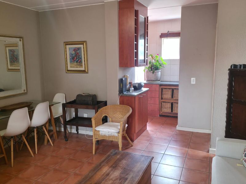 Open plan living and dining area featuring tiled flooring and a compact kitchen with built-in cabinetry and tiled backsplash.
