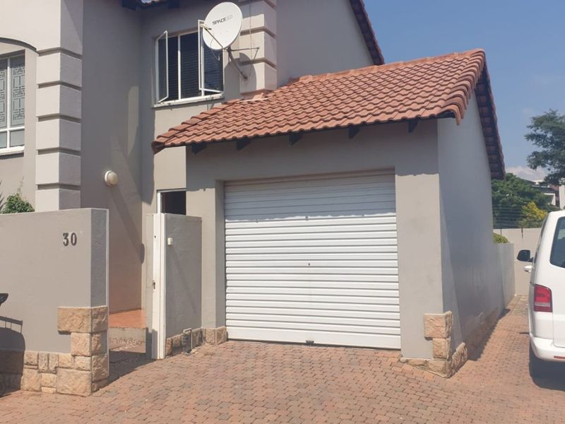 Front elevation of the apartment featuring a single garage, paved driveway, and tiled roof with stone cladding accents.