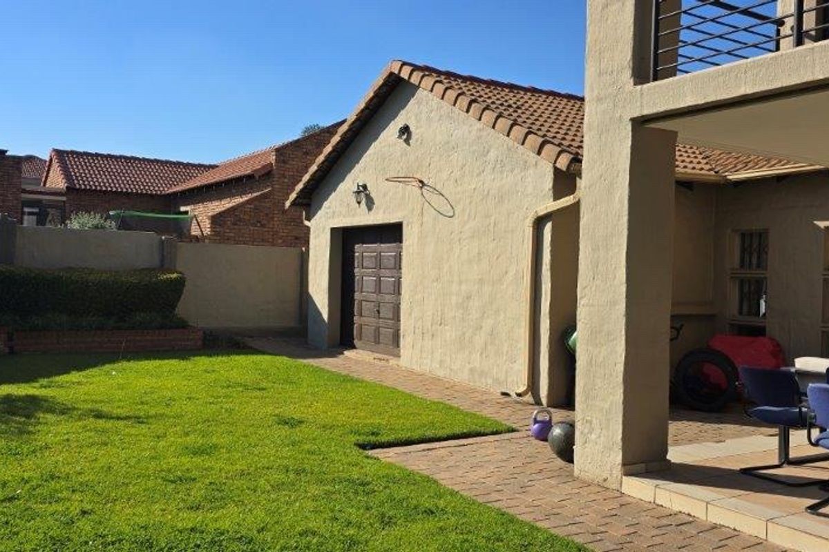 Rear view of the property featuring a well-maintained lawn, paved patio area, and access to the garage.