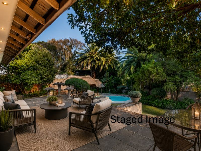 A spacious covered patio featuring stone paving and recessed lighting, overlooking a private swimming pool and lush landscaped garden area.
