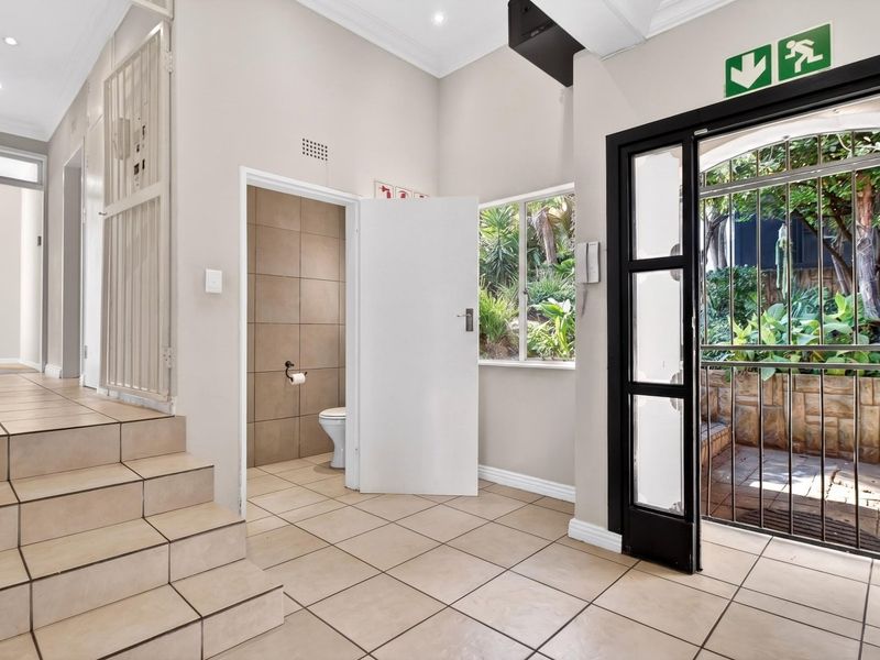 A bright, tiled entrance area featuring a built-in guest toilet, security gate, and direct access to an outdoor garden space.