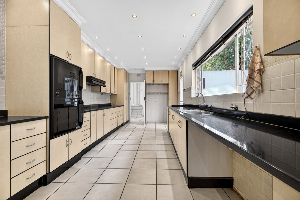 Spacious galley-style kitchen featuring extensive built-in cabinetry, granite countertops, double sink, and integrated oven, finished with neutral floor tiles and recessed lighting.