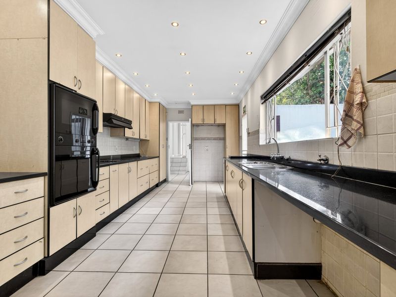 Spacious galley-style kitchen featuring extensive built-in cabinetry, granite countertops, double sink, and integrated oven, finished with neutral floor tiles and recessed lighting.