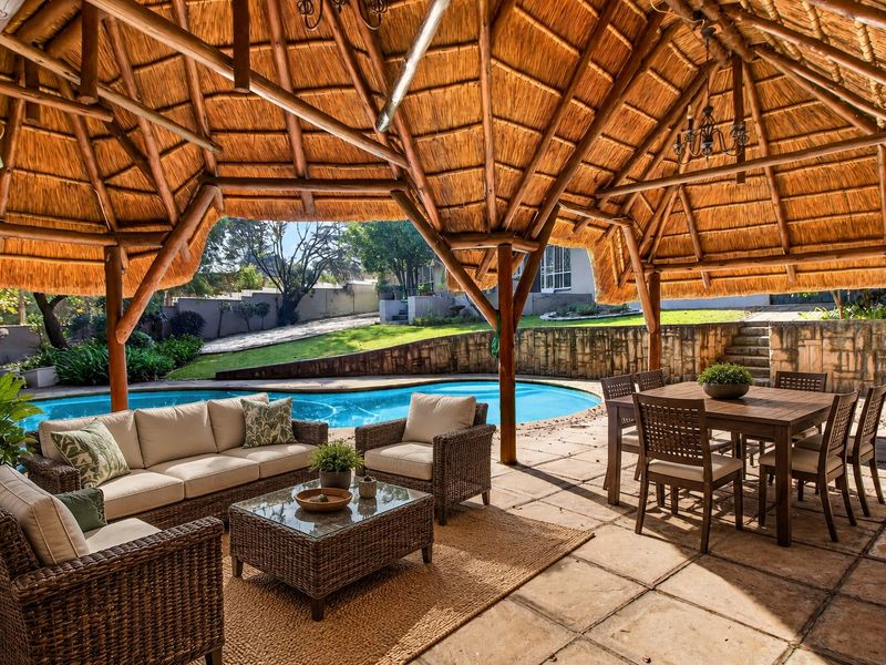 Spacious covered patio featuring a traditional thatched roof and timber supports, overlooking a private swimming pool and landscaped garden area.