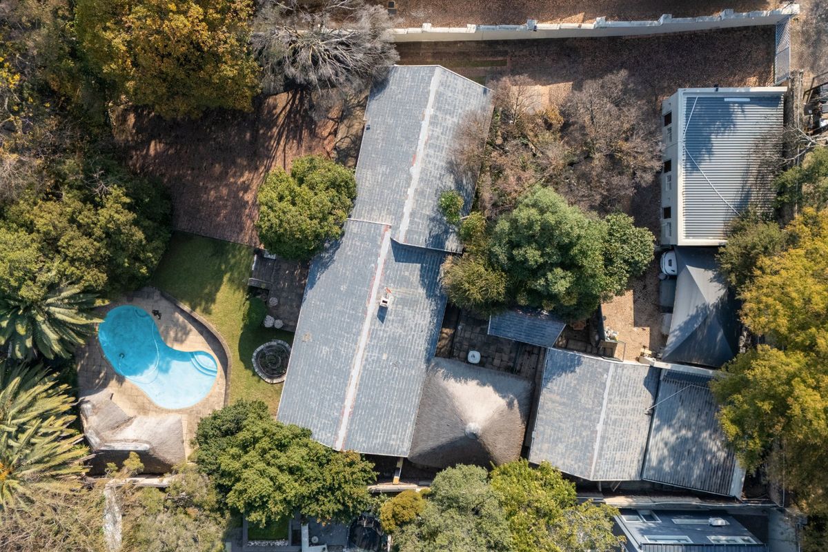 Aerial view of the property showcasing the main dwelling with metal and thatched roofing, a swimming pool, and established garden surroundings.