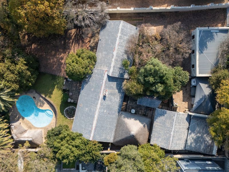 Aerial view of the property showcasing the main dwelling with metal and thatched roofing, a swimming pool, and established garden surroundings.