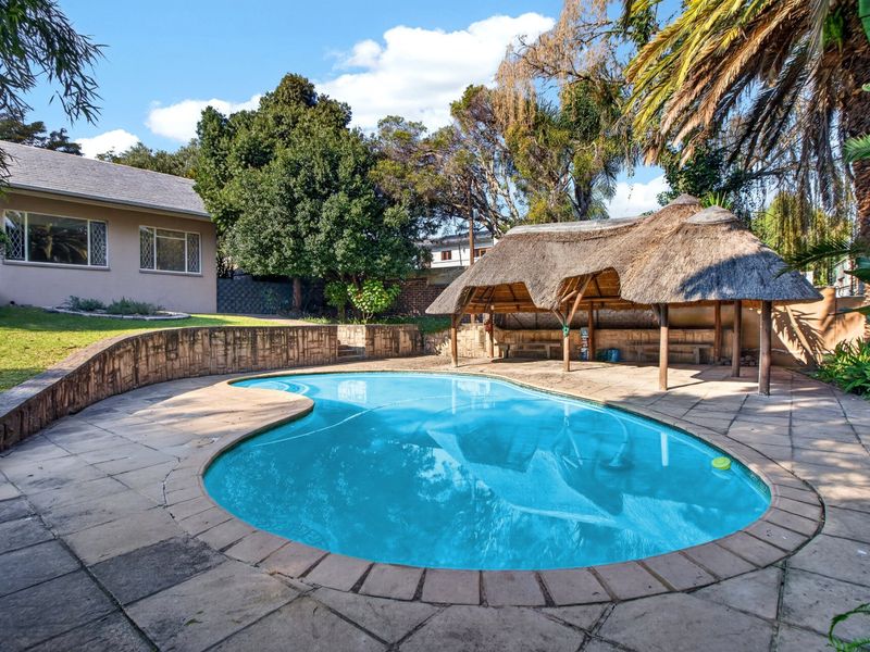 Outdoor pool area featuring a swimming pool, paved surround, stone retaining wall, and a traditional thatched lapa entertainment structure.