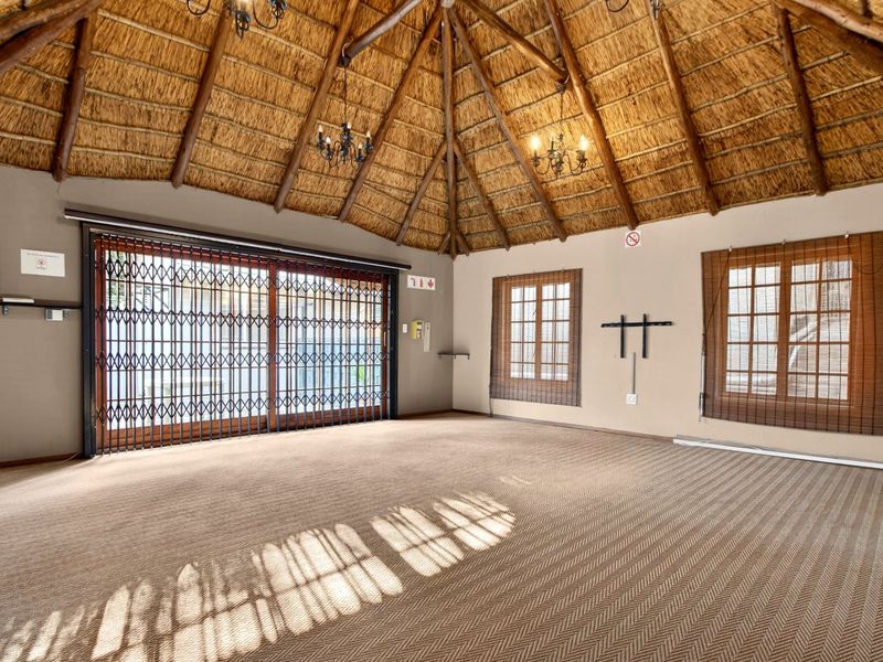 Spacious living area featuring a high vaulted thatched ceiling with exposed timber rafters, carpeted flooring, and large sliding doors with security gates.