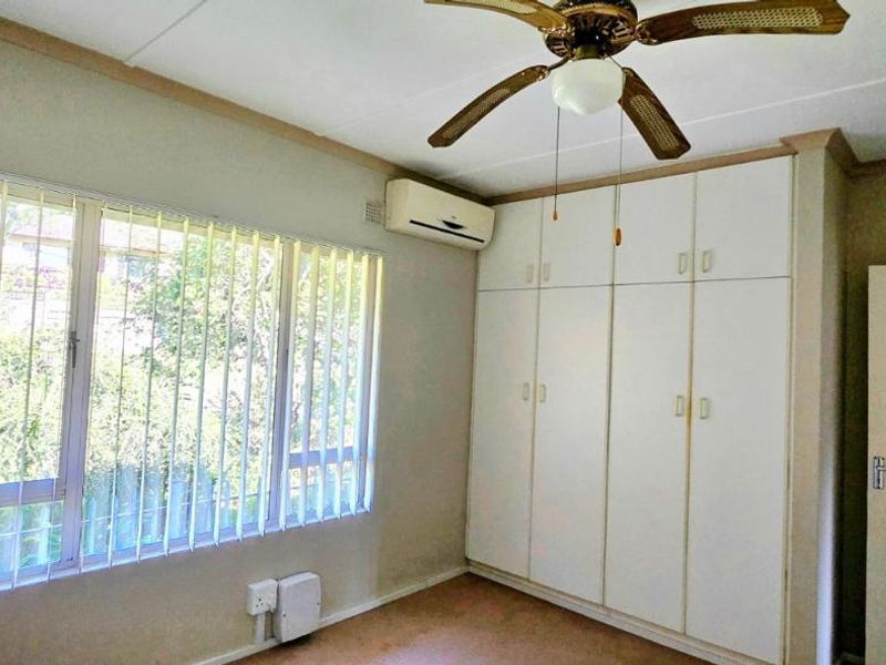 A functional bedroom featuring built-in cupboards, a ceiling fan, and a wall-mounted air conditioning unit, offering a blank canvas for potential updates.