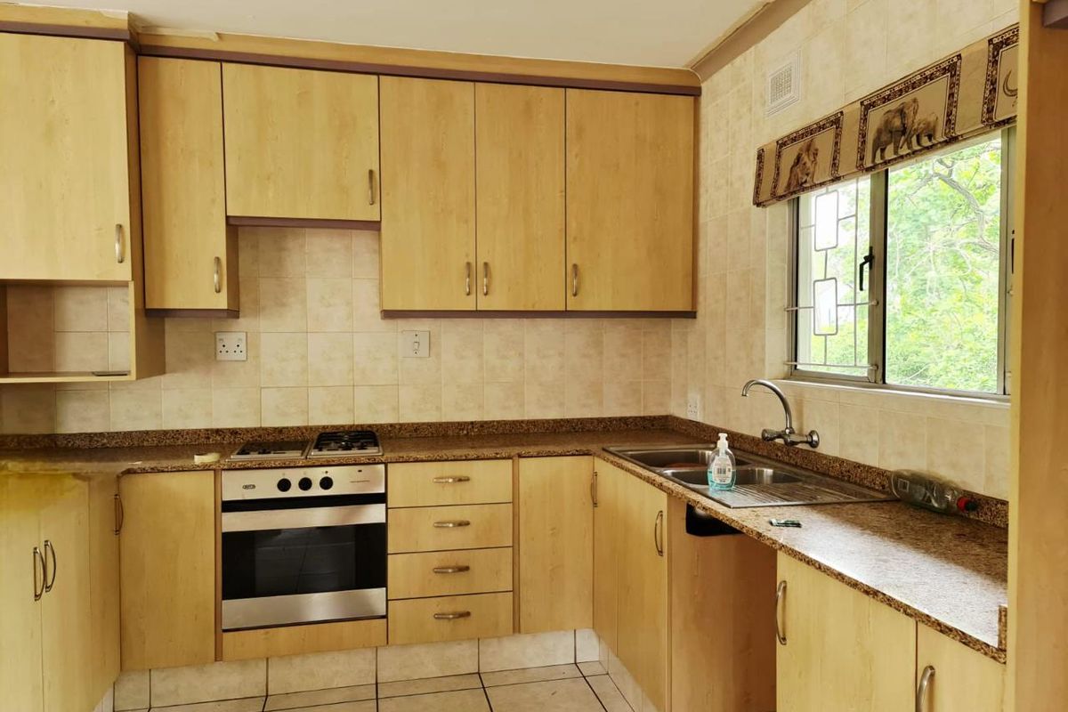 A functional kitchen featuring laminate cabinetry, granite countertops, a built-in oven with gas hob, and a stainless steel sink with a window view.