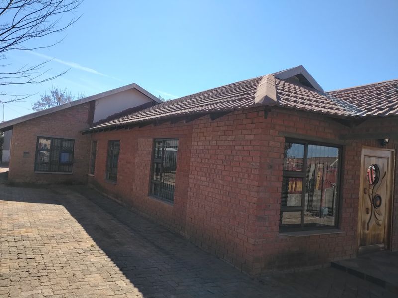 A front exterior view of a face brick house featuring a tiled roof, paved driveway, and secure window fittings.